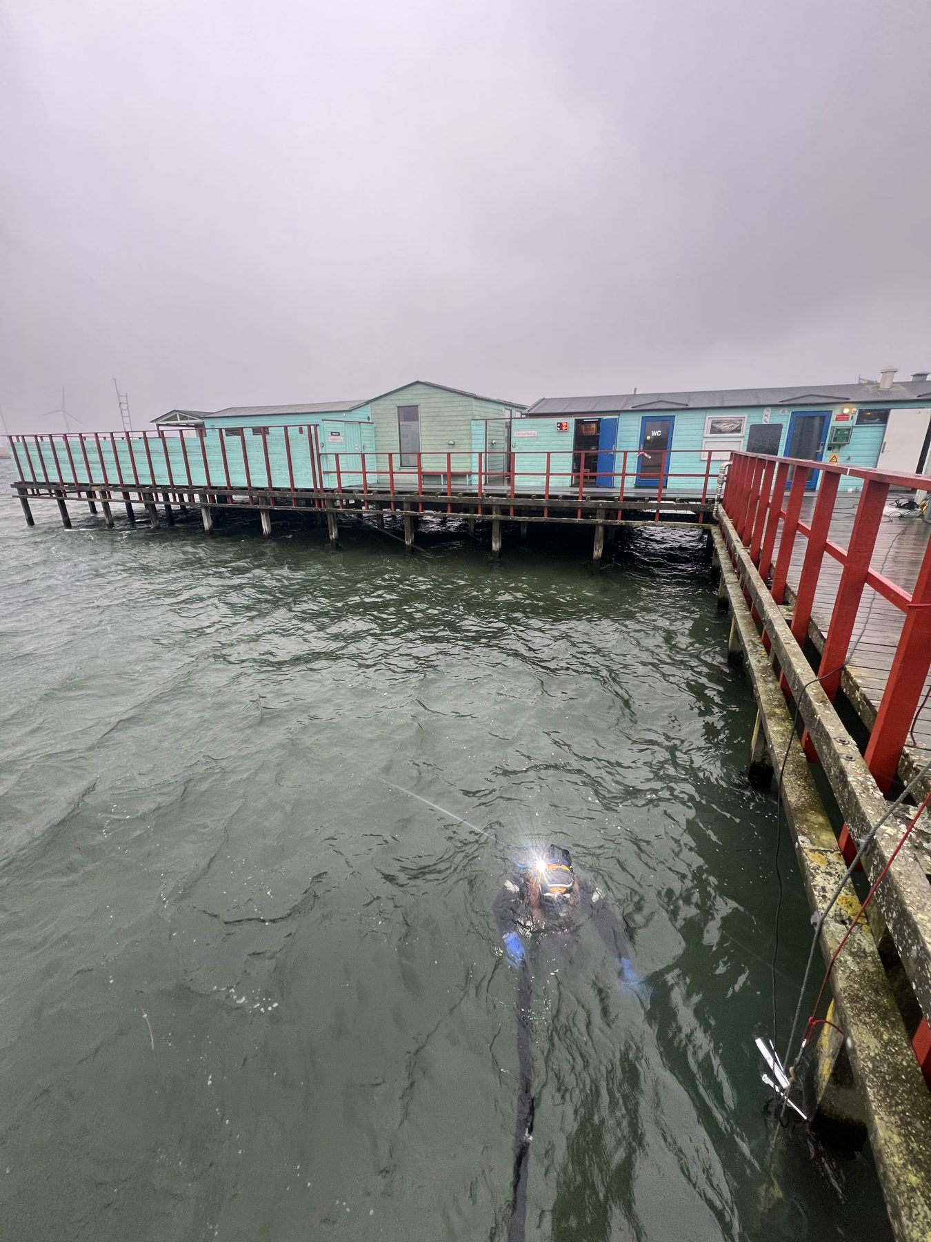 Diver with a lamp in the water beside a bathing jetty in grey weather